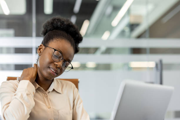 istock Woman in office experiencing neck pain while working on laptop, looking stressed. Overworked employee dealing with discomfort during workday. 2180958286