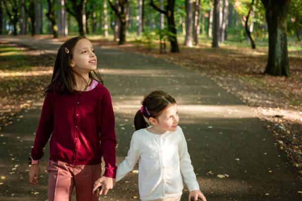 Two little girls are holding hands while walking in the autumn park