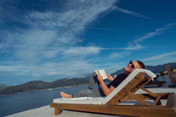 Summertime vacation concept with stacked books and flowers on the balcony with view to the sea horizon