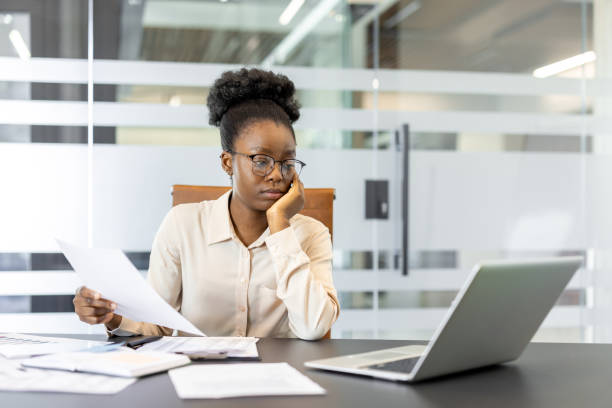istock Businesswoman in office holding documents while working on laptop reflecting focus and diligence in professional environment 2180960550