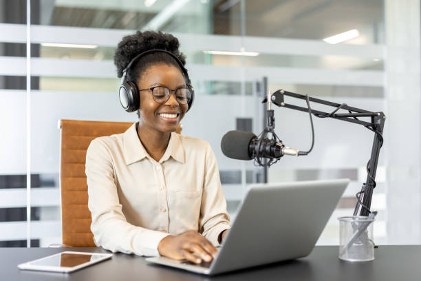 istock Young woman host recording podcast with laptop and microphone in modern office setting, wearing headphones. Engaged and smiling, focusing on creative content creation and communication. 2180963687
