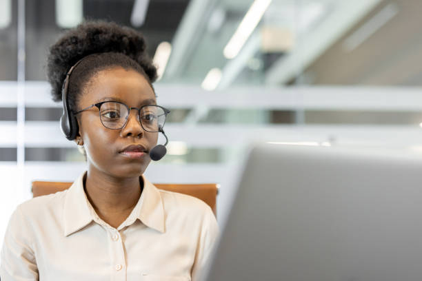 istock Focused woman working with a headset and laptop in modern office environment. Professional concentrated on task through virtual communication, symbolizing remote work and digital technology. 2180964686