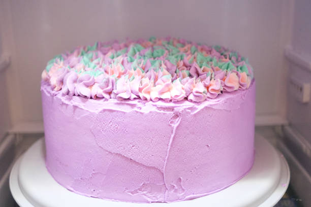Pink birthday cake being frosted with brightly colored icing for birthday party