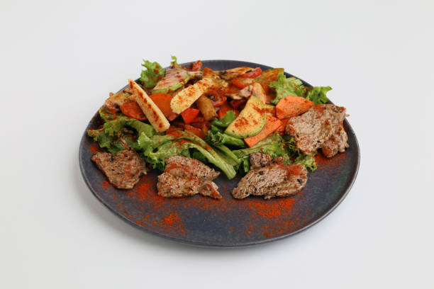 istock Salad with grilled veal and vegetables on a dark plate on a white background, restaurant serving 2180975451