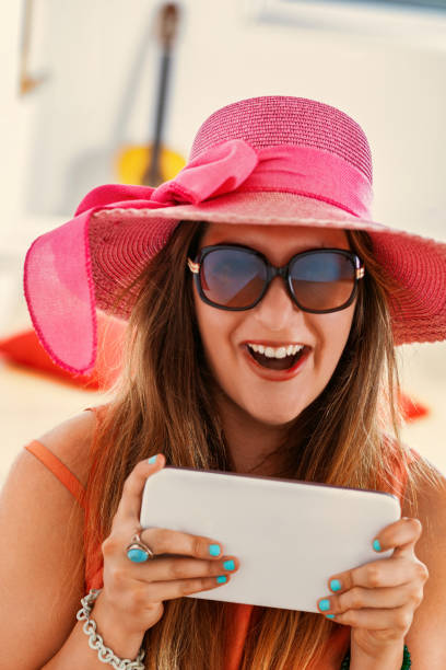istock Excited woman wearing a pink sun hat using a digital tablet at h 2180981167