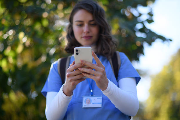 istock Beautiful nurse in uniform holding smartphone in hands, scrolling, looking at device screen. 2180981356
