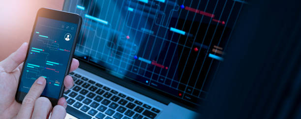 istock A close-up of a hand holding a smartphone displaying a data management interface, with a laptop screen in the background showing a similar data chart. 2180990556