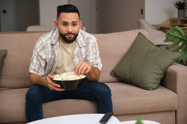 istock Handsome young man eating popcorn and watching tv at home 2180994345