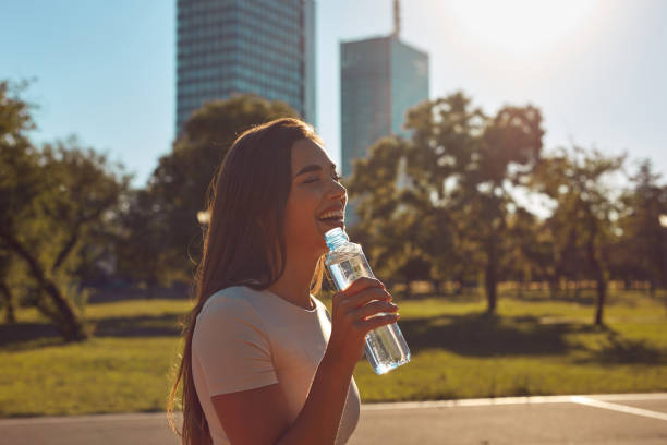Young woman drinking water after jogging and exercise in urban park.