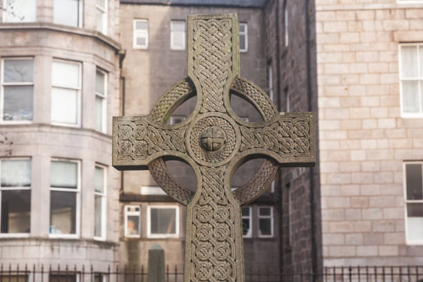 An ancient stone religious cross against the backdrop of a building.