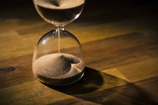 istock Hourglass on wooden table with a black background, sand flowing through the bulb 2180996353