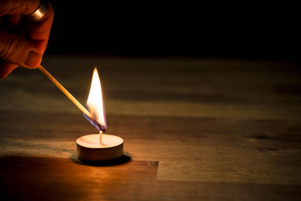 Male hand lighting a small white tea candle on a wooden table, close up shot. Tealight ambiance concept.