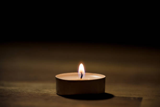 Small white tea candle on a wooden table, close up shot. Tealight ambiance concept.