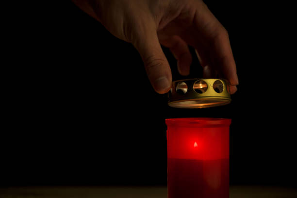 Male hand, using a safety match, lighting a red cemetery candle, on a black background, close up shot. All saints day concept.