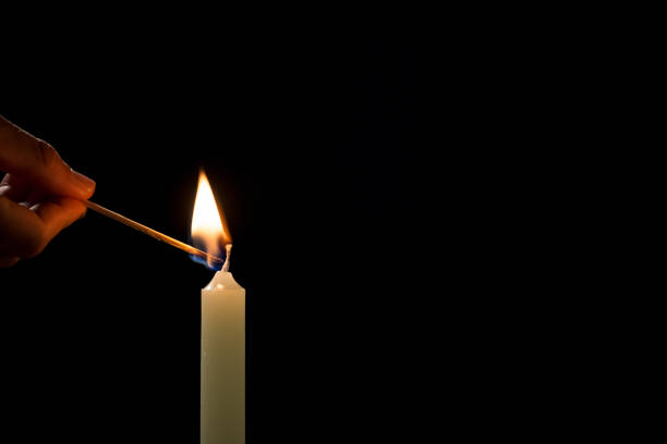istock Male hand lighting a white candle with a match, on a black background 2180996745