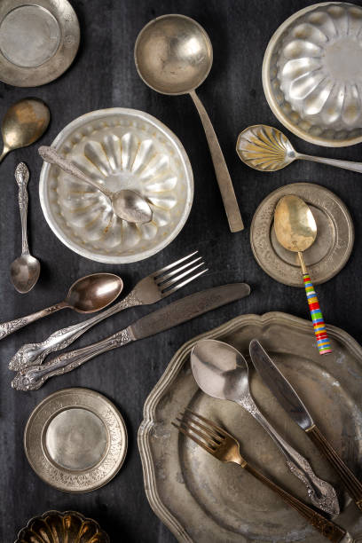 Vintage pewter plates, bowls and cutlery on black chalkboard background. Flat lay. Top view. Food concept. Dark mood food photography.