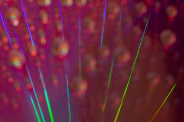 This macro photograph captures a stunning array of diagonal light streaks in vibrant green and purple hues, set against a blurred background with bokeh effects. The abstract composition and vivid colors make it an eye-catching piece, perfect for themes related to technology, optics, or artistic representations.