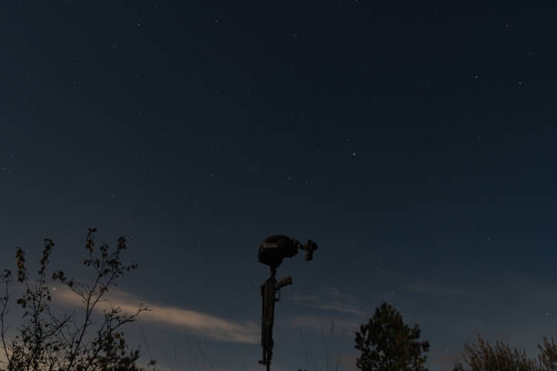 Fallen modern warrior background concept with military helmet with night vision device and assault rifle against the background of the starry sky at night in the forest.Low light photo
