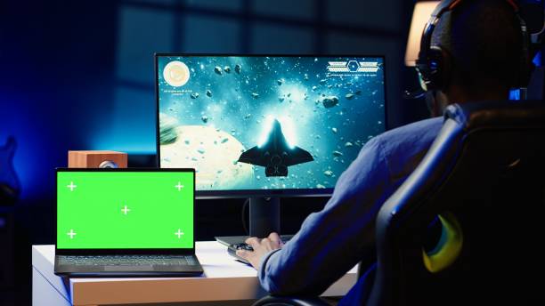 istock Mockup laptop on desk next to man playing SF videogame 2181003739