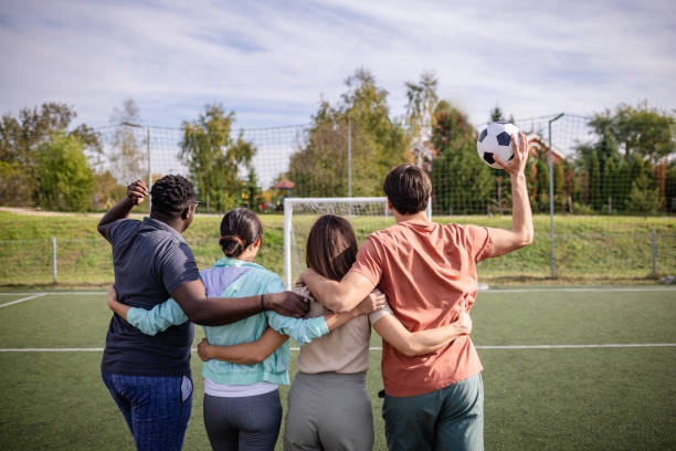A diverse group of people stands together on a soccer field, embracing each other in a display of camaraderie and teamwork as they prepare for a game.