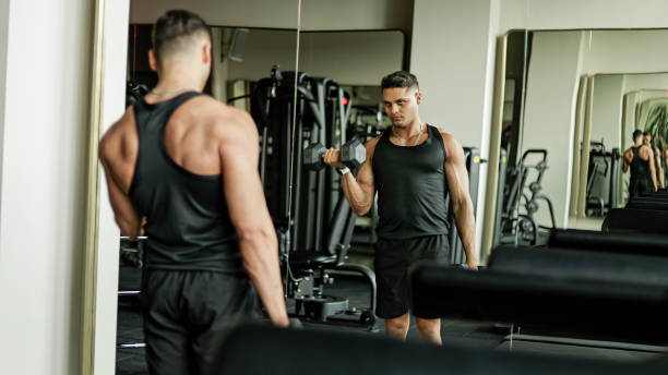 istock Fitness Enthusiast Perfecting His Form with Concentrated Bicep Curls Using Free Weights, Intense Strength Training Session with Muscular Athlete Performing Dumbbell Curls in a Gym Mirror Setting, Highlighting Muscle Strength and Control During a Workout 2181011613