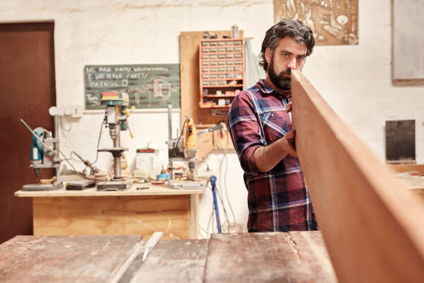 istock Carpenter expertly checking a wooden plank for straightness and 2181014474