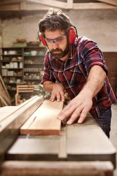 istock Carpenter wearing protective gear cutting a plank of wood 2181015453