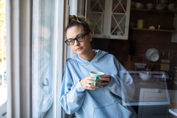istock Young woman having a cup of coffee while looking through a window at home 2181030699