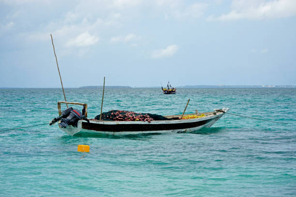 Zanzibar, Tanzania - 08 August 2025: Sailing boat on the coast of Zanzibar at Nungwi beach paradise resort. Fishermen and women doing traditional fishing at the sea shore. White sand beach and boats
