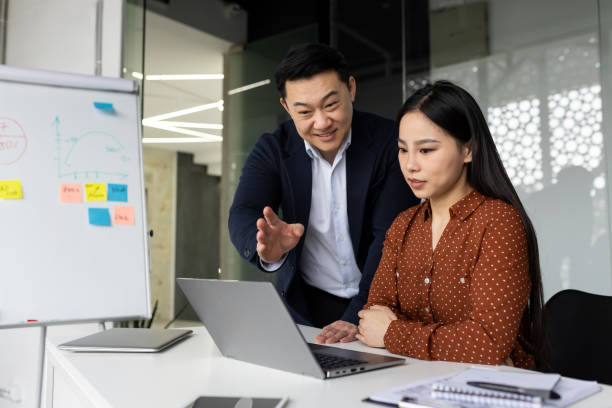 istock Business professionals collaborating on laptop in modern office setting, with mentor guiding colleague during work meeting for project planning 2181047343