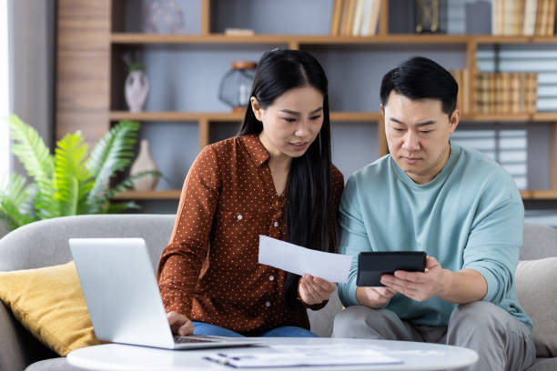 istock Couple calculating expenses together at home using a calculator and laptop, focused on financial planning and budgeting 2181049417