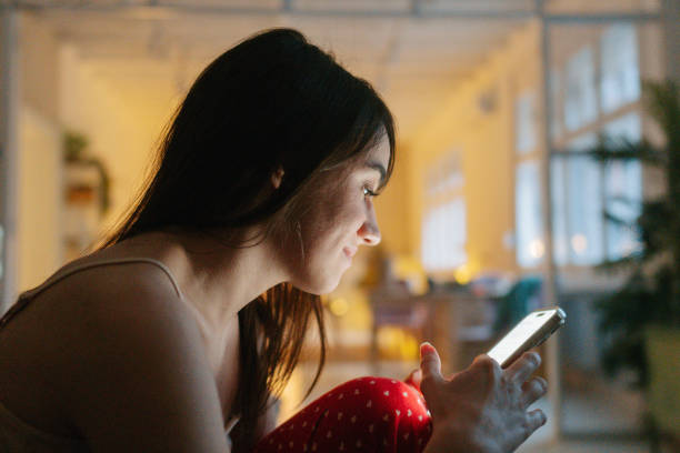 Photo of a young woman using mobile phone and checking her social media accounts while in bed.