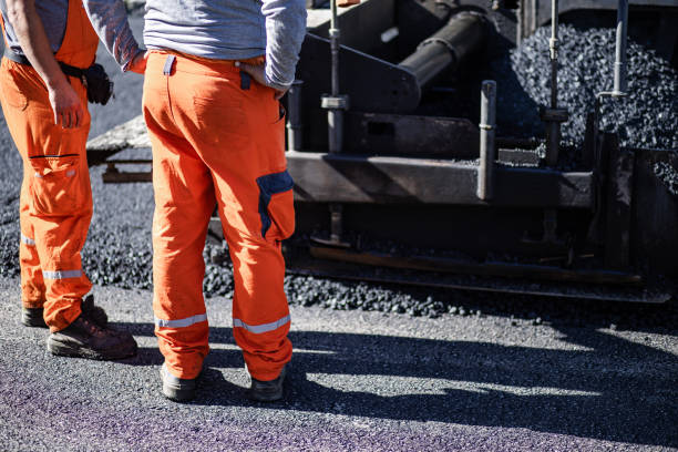 istock Construction workers in bright orange uniforms supervise asphalt paving on a sunny day at a road construction site 2181059464