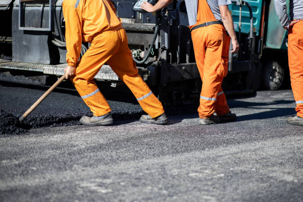 istock Construction workers laying asphalt on a road in bright orange uniforms during daytime in a busy urban area 2181059494