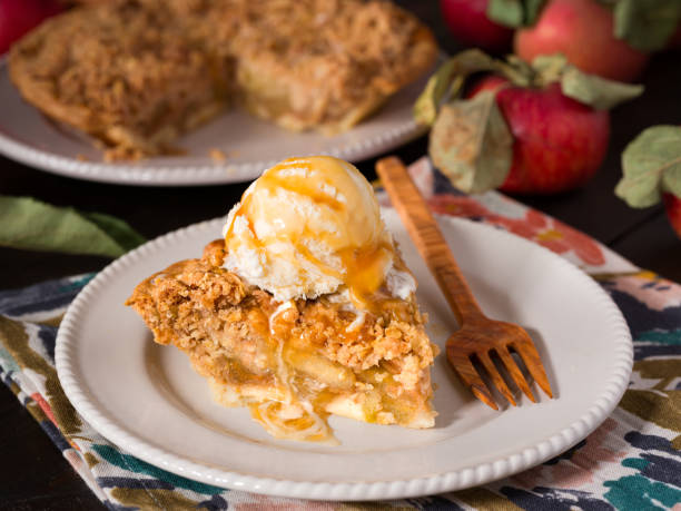 Slice of apple crumb pie topped with a scopp of vanilla ice cream surrounded by fresh picked apples Close-up of a slice of apple crumb pie in a white plate with fresh picked apples apple pie and ice cream stock pictures, royalty-free photos & images