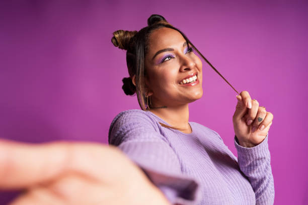 Smiling influencer creating social media content and taking selfie with smartphone against a vibrant purple backdrop