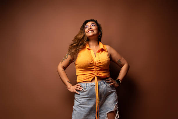 Plus size woman smiling and looking up with hands on hips Studio portrait of a beautiful plus size woman smiling and looking up with hands on her hips, expressing confidence and body positivity free tatto designs stock pictures, royalty-free photos & images