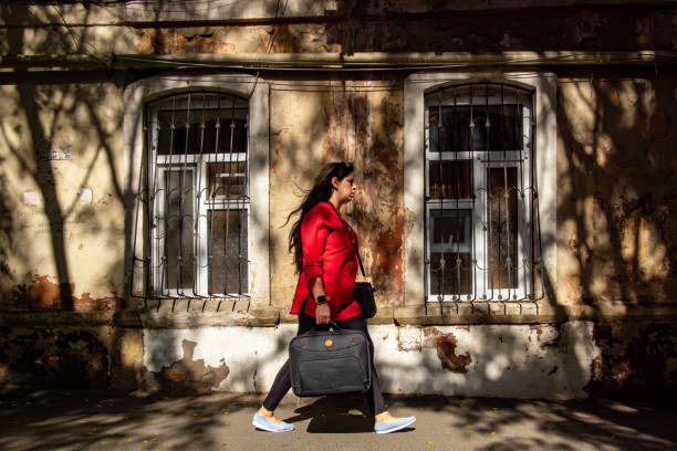 Baku, Azerbaijan Sept 22, 2024 A female pedestrian in a red jacket  walks on the sidewalk on tree-lined street with strong shadows.