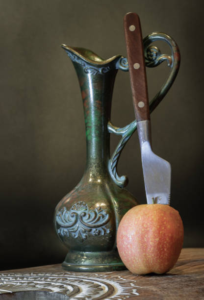 istock A knife is inserted into Naturally pink fresh kissabel apple fruit with Antique iron jug on wooden cutting board. 2181068355
