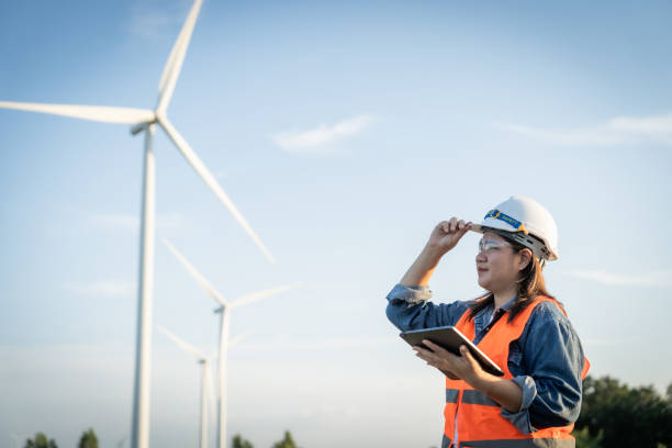 istock engineer wearing a hard hat and safety vest is looking at a tablet while standing in front of a wind turbine 2181068769