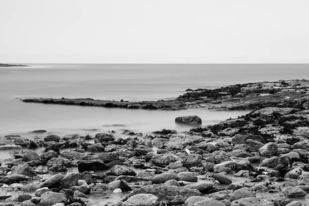 bay surrounded by a wide curve of rock and cliff, beach and wave, shot in monochrome