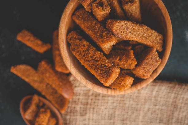 Wooden bowl filled with crispy rye croutons placed on a burlap cloth, creating a rustic snack presentation.