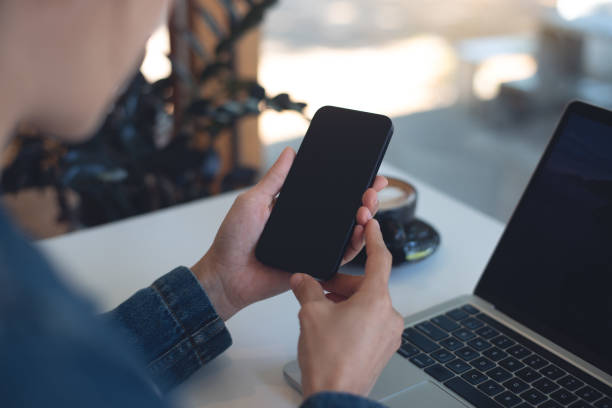 istock Cell phone black screen mockup, Woman hand holding mobile phone with blank screen while working at coffee shop. Business woman using smartphone, mockup for social media marketing 2181089241