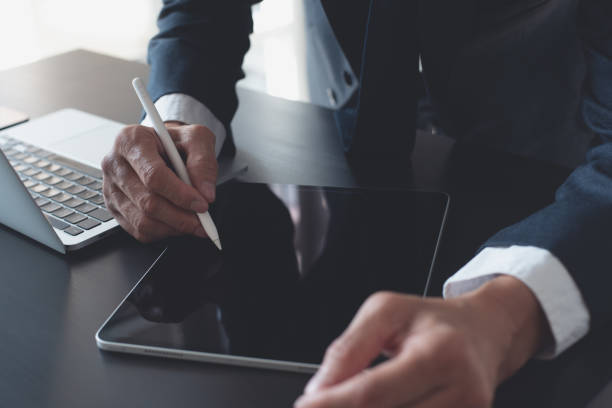 istock Businessman hand using stylus pen touching on digital tablet screen with laptop computer on office table. Business man signing e-document on tablet, online working at office, close up 2181095060