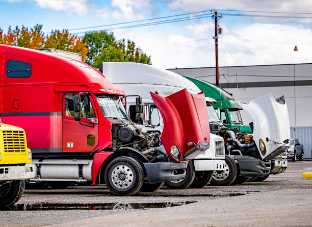 Big rig semi trucks tractors with open hoods standing in row on industrial parking lot waiting for engine repair and transmission maintenance stock photo