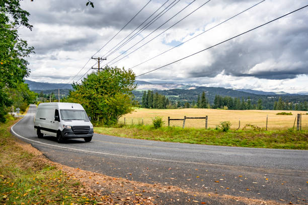 istock Compact white cargo mini van making local delivery running on the winding road with summer meadow on the side 2181106813