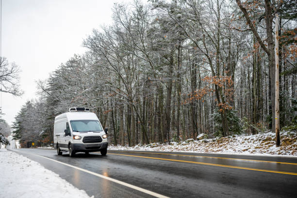 istock Commercial cargo mini van with refrigerator unit on the roof transporting cargo running on the wet slippery winter road with snowy forest on the side 2181106952