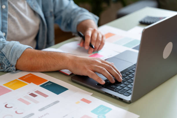 Designer working on laptop taking notes with colour palette on desk