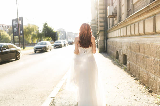 Rear view shot of bride walking in the city on sunny day