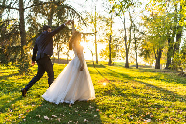 Full length shot of beautiful bride and groom dancing in park on sunny autumn day